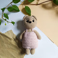 Cute crocheted plush toy in pink dress on pastel background