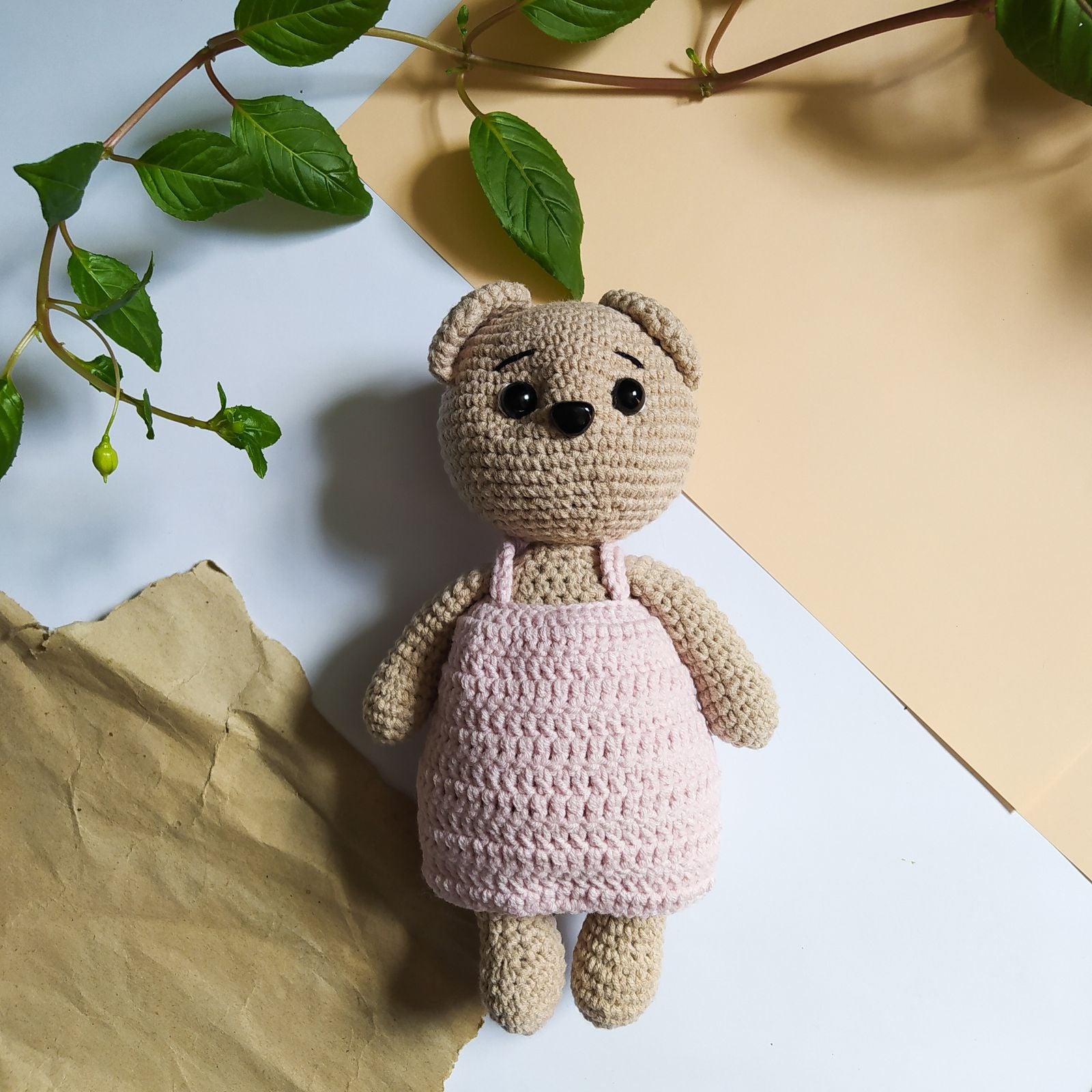 Cute crocheted plush toy in pink dress on pastel background