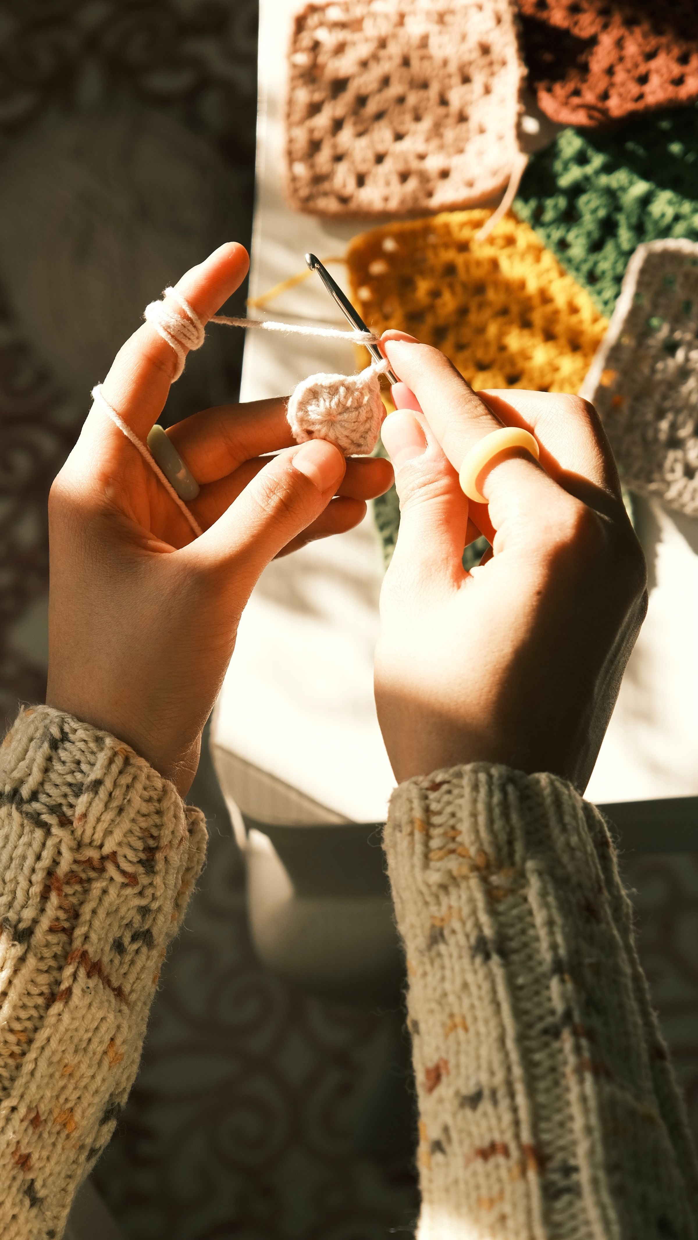 Hands crocheting colorful granny squares in warm sunlight
