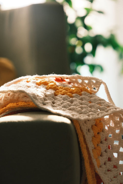 Handmade crochet blanket draped over a sofa in warm sunlight
