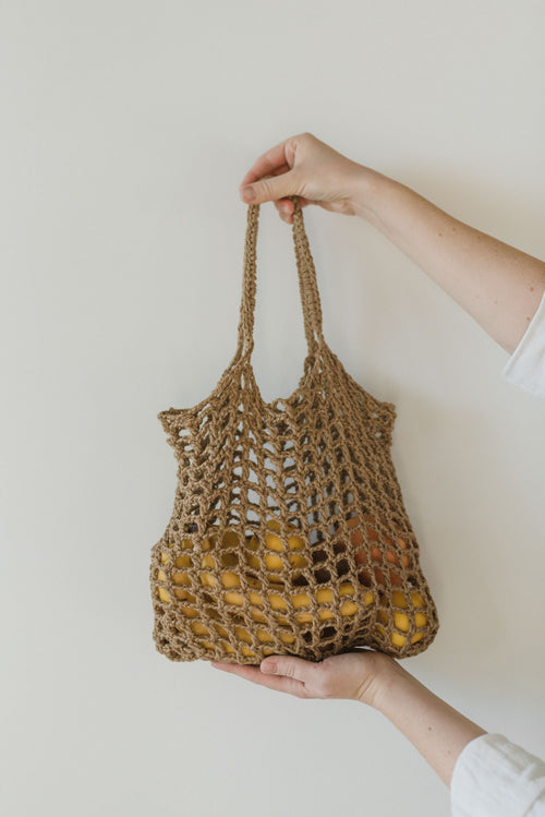 Hand holding crocheted market bag filled with yellow fruits